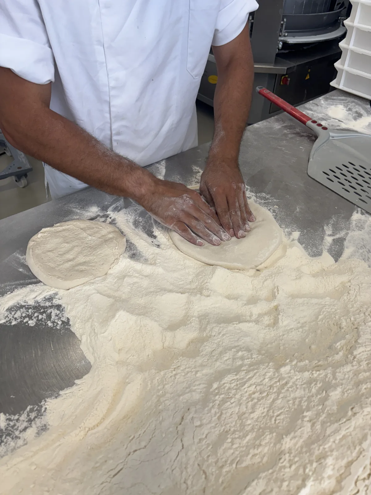A pizzaiolo hand-stretching a pizza base on the floured bench